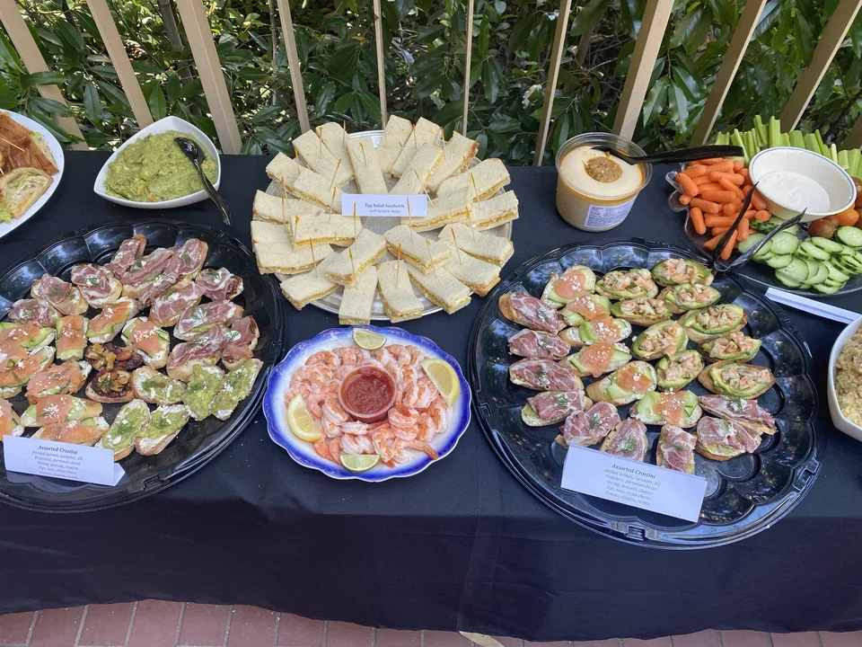 Another table with several trays of food, including sandwiches and other sides.
