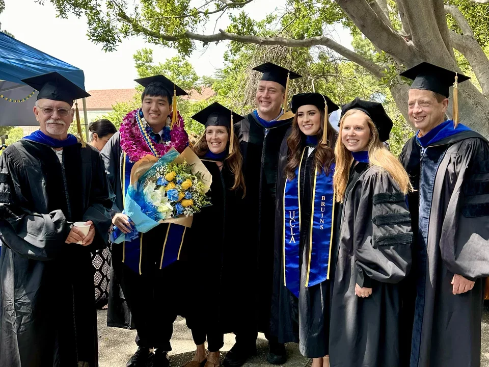 Several faculty and students stand together for a group photo. They are dressed in graduation gowns!