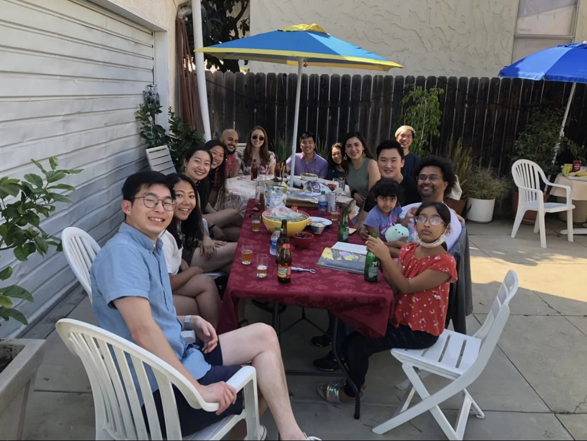 The entire lab plus extended friends and family gather around a long picnic table in Peter’s backyard.