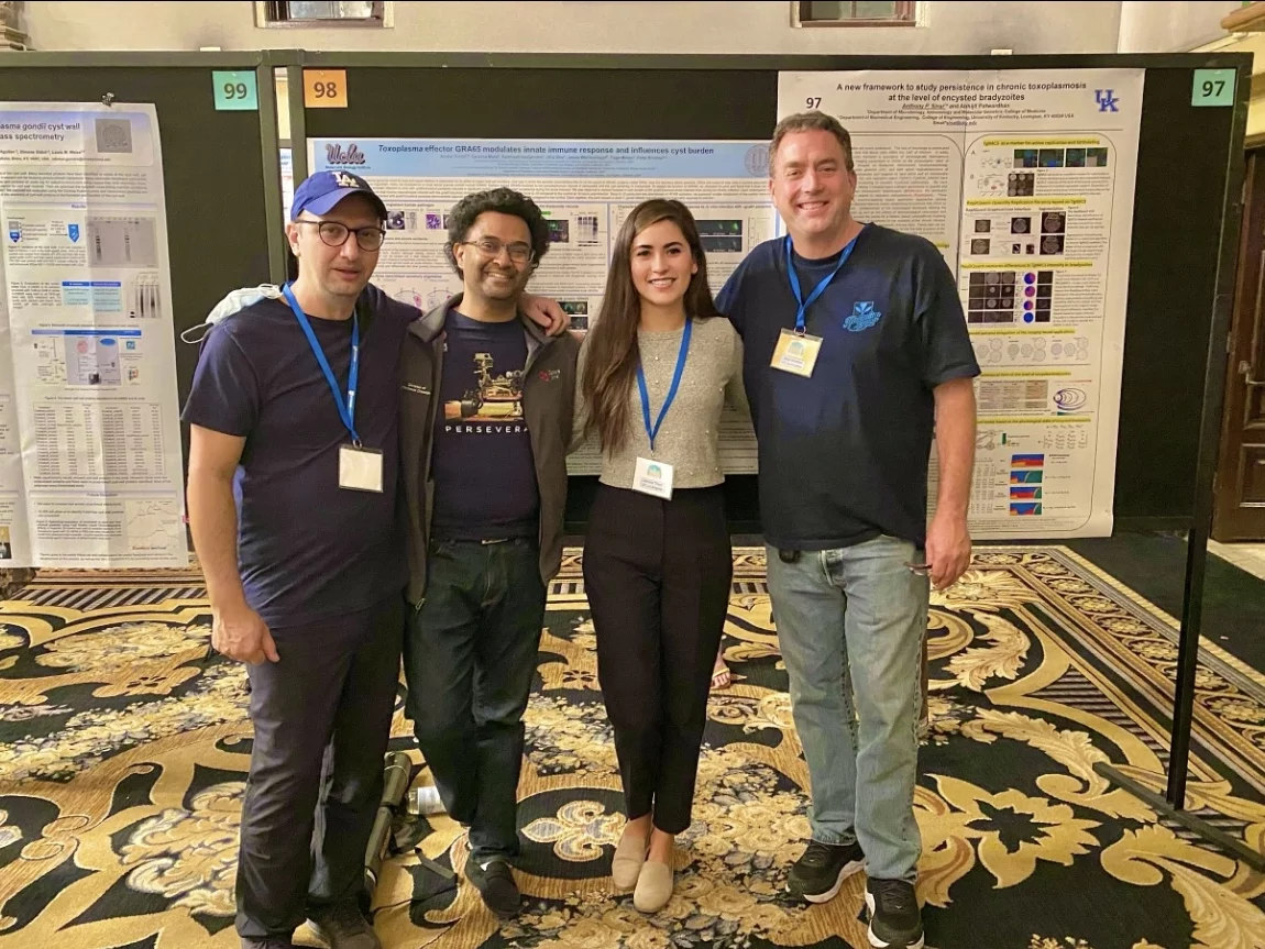Four lab members stand in front of large posters at a parasitology conference.